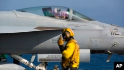 A crew member signals to a pilot in an F/A-18 fighter jet on the deck of the USS Abraham Lincoln aircraft carrier in the Arabian Sea, Monday, June 3, 2019. 