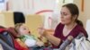 Nevelt gyermekét eteti egy nő a Befogadlak nevelőszülő-programot népszerűsítő kampány győri állomásán (képünk illusztráció)