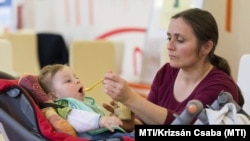 Nevelt gyermekét eteti egy nő a Befogadlak nevelőszülő-programot népszerűsítő kampány győri állomásán (képünk illusztráció)