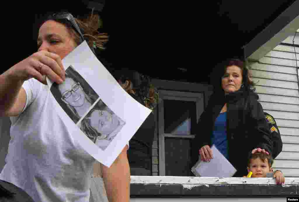 Patty Campbell (top right), the mother of blast victim Krystle Campbell, looks out from her porch while a neighbor (left) hands out copies of photos of her daughter in Medford, Massachusetts, on April 16, 2013.