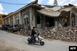 A youth rides a moped past a mosque that was hit by a recent Israeli strike in the southern Lebanese village of Kfar Sir.