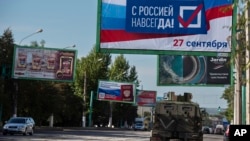 Një makinë ushtarake në Luhansk të Ukrainës, shihet afër një panoje në të cilin thuhet: "Me Rusinë përgjithmonë".