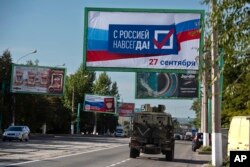 Военная машина армии РФ проезжает по улице, где размещены рекламные щиты с агитацией принять участие в так называемых референдумах на оккупированной Россией части Украины, 22 сентября 2022 года