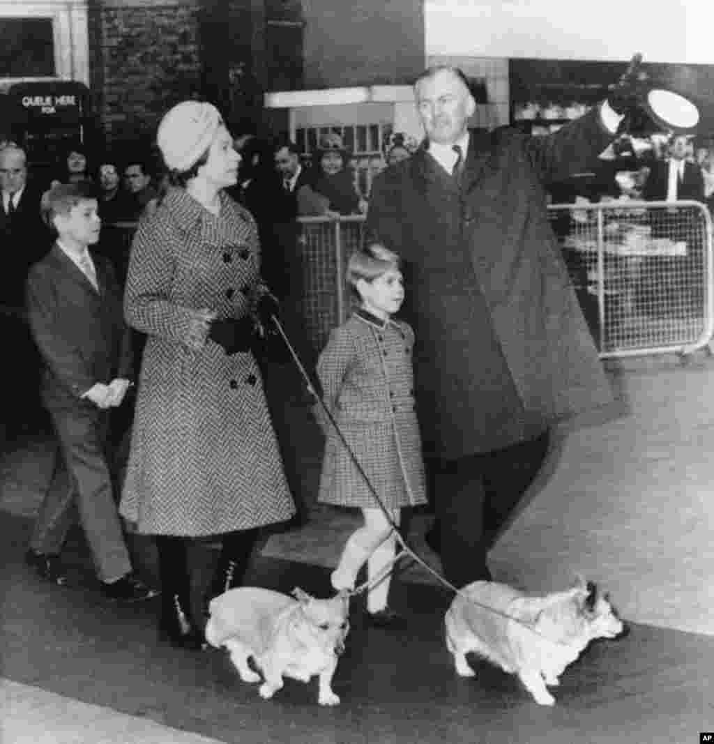 Regina Elisabeta a II-a a Marii Britanii este însoțită de doi dintre fiii ei, prințul Andrew, în vârstă de 10 ani, în stânga, și prințul Edward, în vârstă de 6 ani, și de doi dintre corgi regali, în timp ce discută cu un oficial în gara Liverpool din Londra, la 30 decembrie 1970. &nbsp;