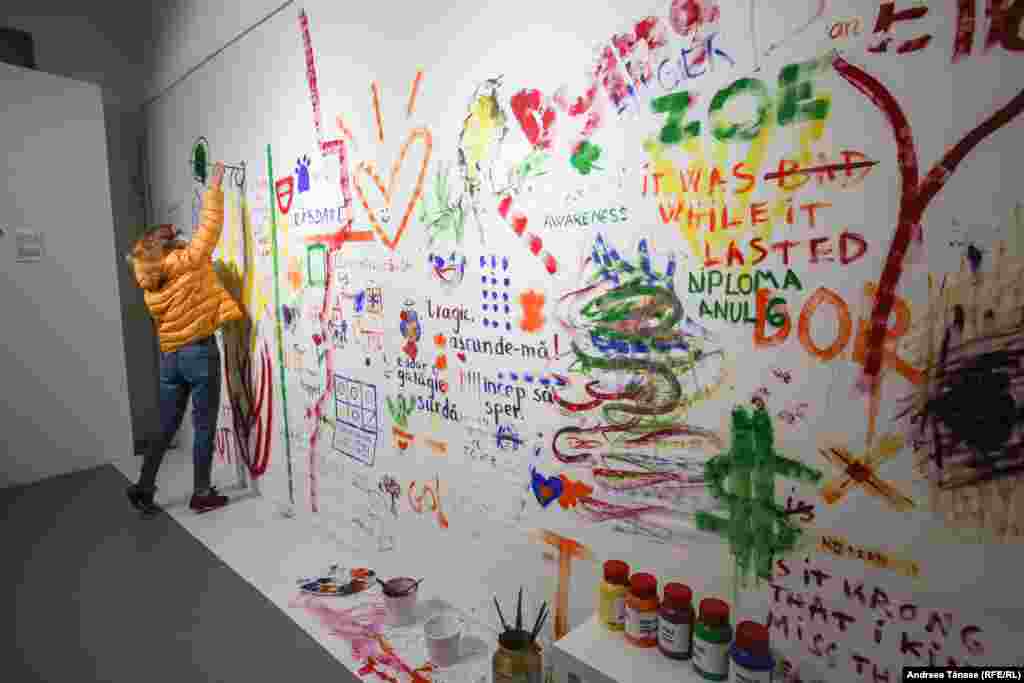 O femeie pictează pe un perete dedicat mesajelor vizitatorilor, în cadrul expoziției &bdquo;Identități Fragile&rdquo; &ndash; Muzeul Pandemiei.&nbsp;