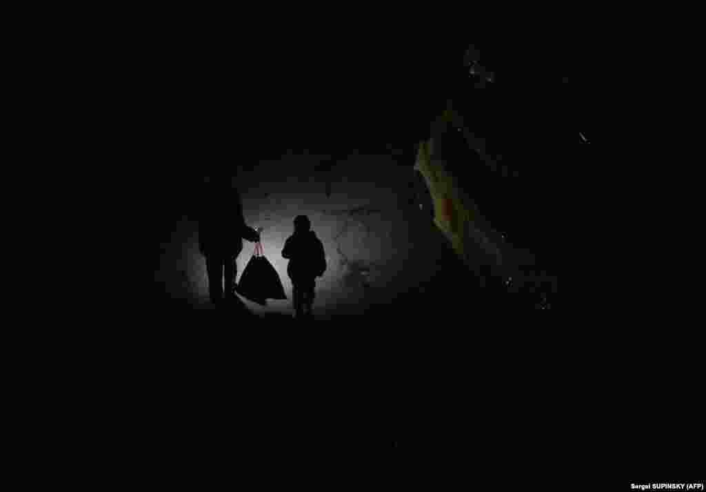 A Ukrainian man shines a flashlight as he and his son walk down a dark street during a blackout in Kyiv.