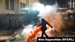  Маскиран служител на реда рита димна бомба до постройката на Народното събрание на Грузия в Тбилиси на 29 ноември по време на втората нощ на митинги, които избухнаха, откакто грузинското държавно управление разгласи прекъсването на договарянията за присъединение към Европейски Съюз. 