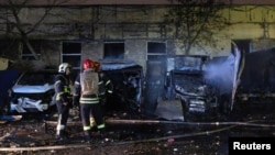 Firefighters stand near burned-out cars at an impact site after a Russian drone attack in Kyiv on November 8.