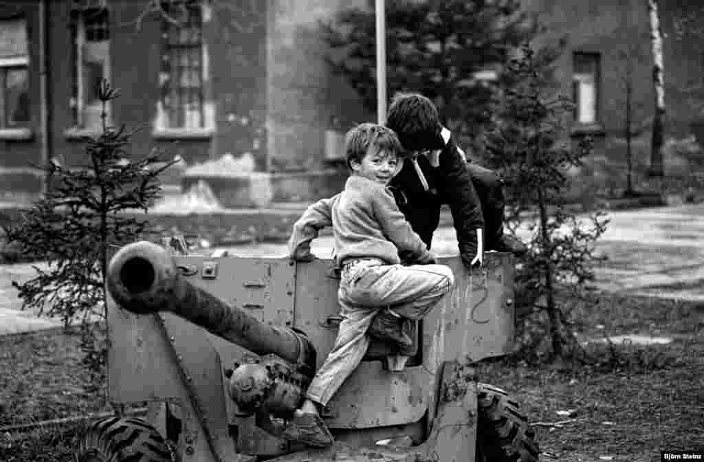 Djeca izbjeglice iz Bosne i Hercegovine u izbjegličkom kampu u Varaždinu, Hrvatska, u zimu 1992. godine. Dječak lijevo je Elvis, na fotografiji u igri sa prijateljem oko topa.