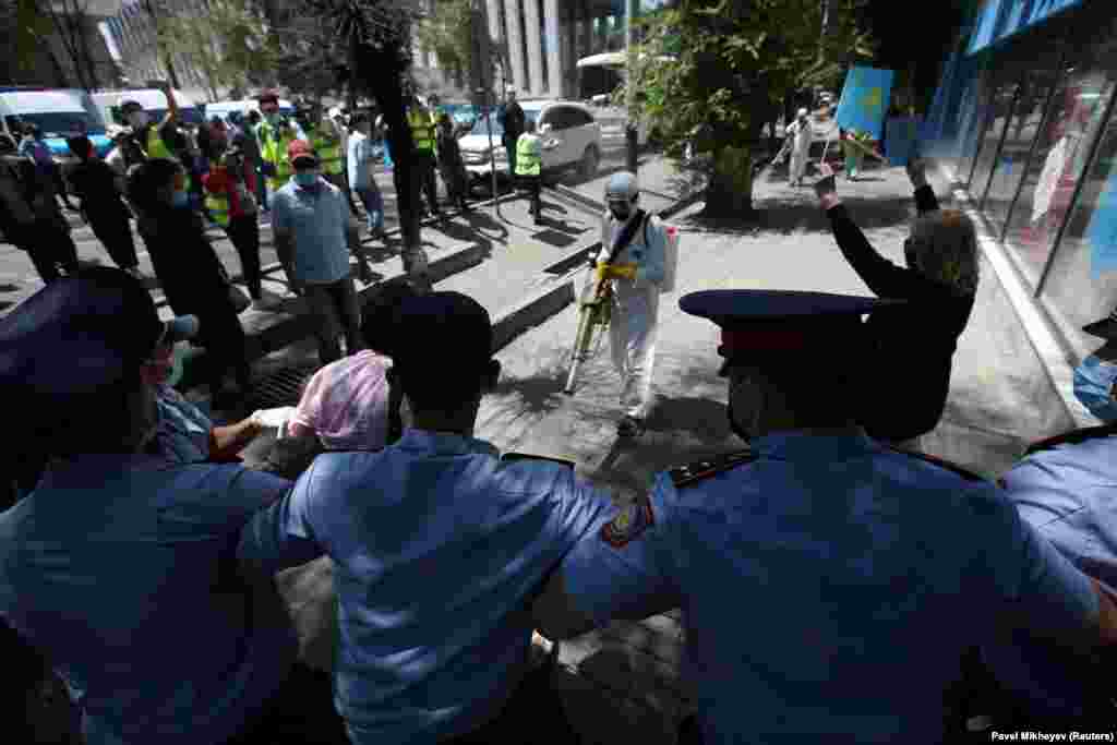 Specialists wearing protective gear spray disinfectant while sanitizing a street to prevent the spread of the coronavirus as police stand guard during an unsanctioned rally in Almaty.