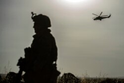 Një ushtar amerikan patrullon teksa një helikopter rus fluturon mbi qytetin sirian al-Maikiyah. 3 qershor, 2020.