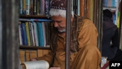 افغانستان - یک کتاب‌فروش در حال خواندن کتاب دیده می‌شود.