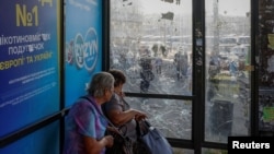 Femei așteptând într-o stație de autobuz avariată de lovituri aeriene rusești la Kiev, pe 10 iulie 2025.