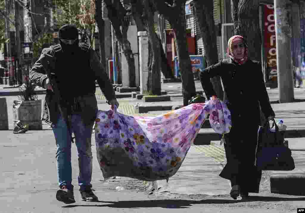 An armed Turkish police officer helps a woman carry her belongings as she leaves her house during clashes in central Diyarbakir on March 17. (AFP/Ilyas Akengin)