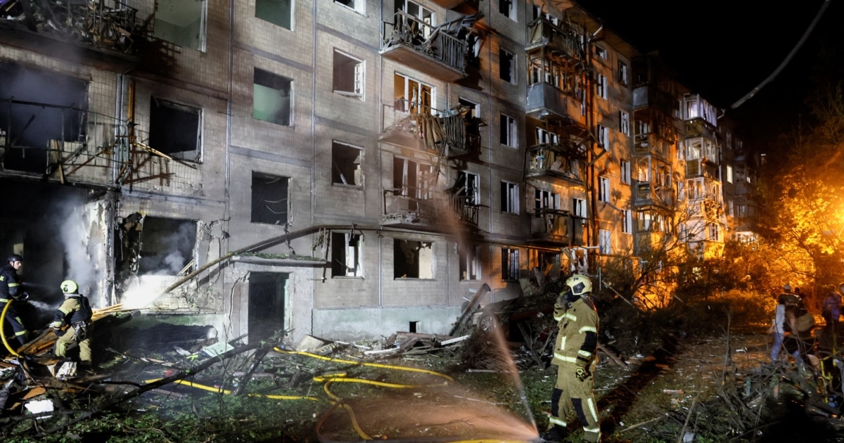 Firefighters spraying water on a burnt apartment building at night