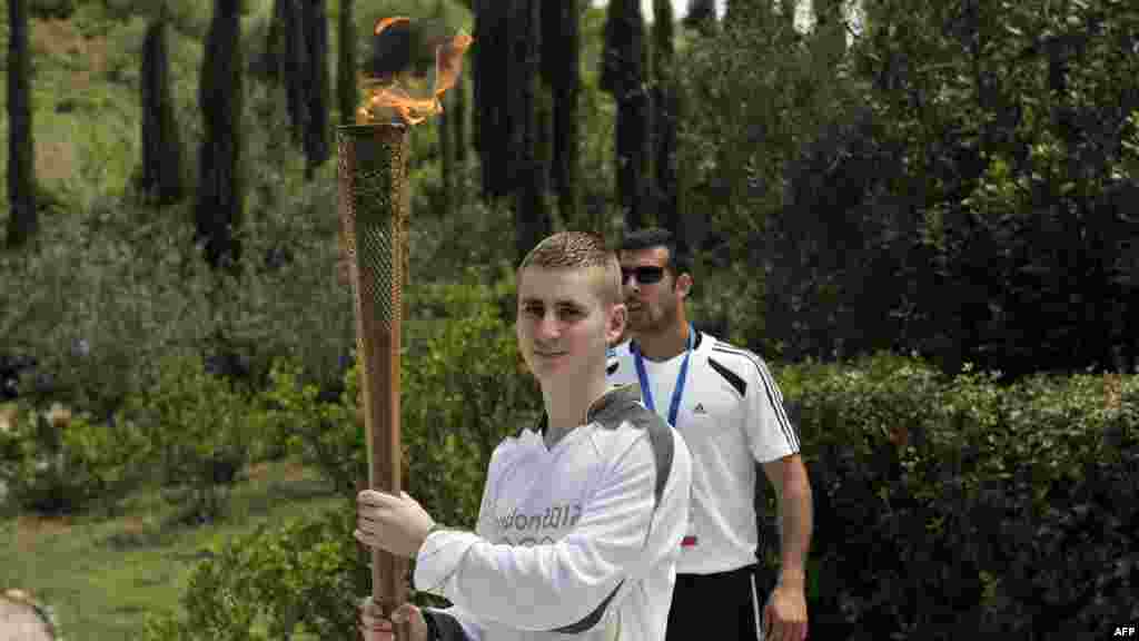 Брытанскі баксёр Аляксандрас Лукас трымае паходню з алімпійскім агнём падчас эстафэты алімпійскага агню пасьля цырымоніі яго запальваньня ў Старажытнай Алімпіі 10 траўня 2012 году.