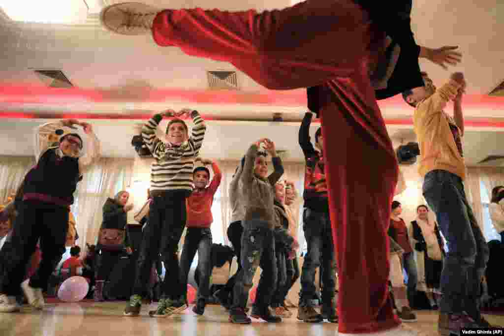 Refugee children mimic ballet dancing along with an entertainer in Bucharest, Romania. Children from families of refugees, coming from Syria, Iran, Iraq, Pakistan, Afghanistan and Congo, took part in an event occasioned by Romania&#39;s national day. (AP/Vadim Ghirda)