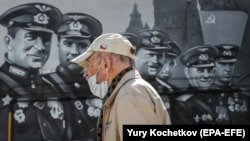 Мужчина в защитной маске идет перед огромным граффити, посвященным победе во Второй мировой войне. Москва, май 2020 года. 