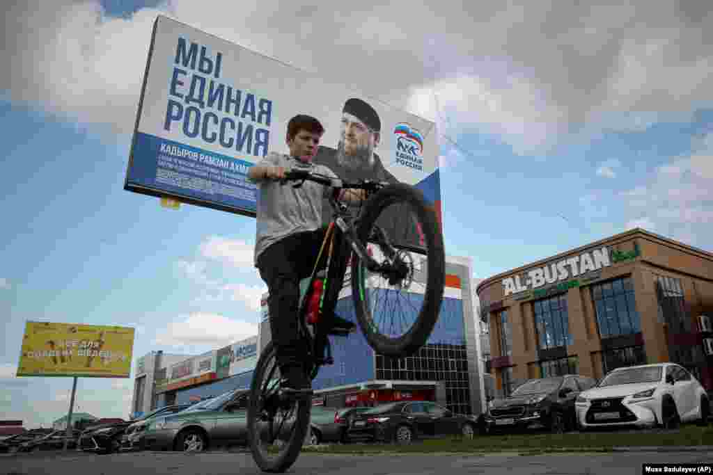 A boy rides his bicycle past an election poster for Russia&#39;s ruling United Russia party with a portrait of Chechen leader Ramzan Kadyrov.
