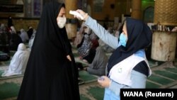 An Iranian woman checks the temperature of a worshipper attending Friday Prayers in a mosque in Qarchak, in Tehran Province, on June 12.