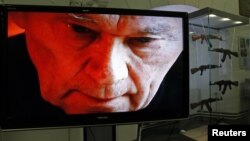 The image of AK-47 inventor Mikhail Kalashnikov is seen on a screen near a display of his weapons during an exhibition at the Artillery Museum in St. Petersburg.