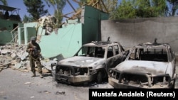 A member of the Afghan security forces stands guard next to damaged army vehicles after a Taliban attack in the city of Ghazni, August 15, 2018.