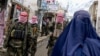 Taliban security personnel stand guard as an Afghan burqa-clad woman walks along a street at a market in northern Afghanistan. (file photo)