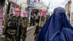 Taliban security personnel stand guard as an Afghan burqa-clad woman walks along a street at a market in northern Afghanistan. (file photo)