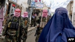 Taliban security personnel stand guard as an Afghan burqa-clad woman walks along a street at a market in northern Afghanistan. (file photo)