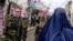 Taliban security personnel stand guard as an Afghan burqa-clad woman walks along a street at a market in northern Afghanistan. (file photo)