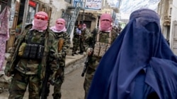 Taliban security personnel stand guard as an Afghan burqa-clad woman (R) walks along a street at a market in the Baharak district of Badakhshan province on February 26, 2024. (Photo by Wakil KOHSAR / AFP)