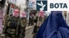 Personeli i sigurisë talibane bën roje teksa një grua afgane e veshur me burka ec përgjatë një rruge në Afganistanin verior. (Fotografi nga arkivi)