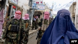 Taliban security personnel stand guard as an Afghan burqa-clad woman walks along a street in northern Afghanistan. (file photo)