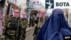 Personeli i sigurisë talibane bën roje teksa një grua afgane e veshur me burka ec përgjatë një rruge në Afganistanin verior. (Fotografi nga arkivi)