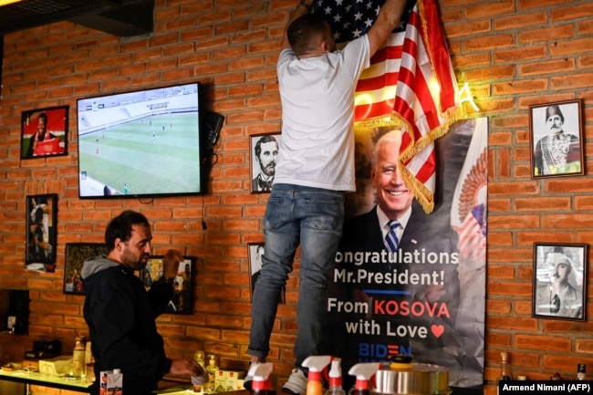 Një banakier shihet duke e vendosur flamurin amerikan afër fotografisë së Joe Bidenit, pak pasi ai i ka fituar zgjedhjet presidenciale të vitit 2020. Nëpër disa sondazhe, Kosova ishte renditur në mesin e vendeve më proamerikane në botë.