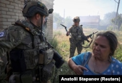 A member of Ukraine's White Angels police evacuation unit holds a fragment of a drone as a resident of Druzhkivka is assisted by a colleague on June 21.