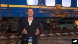 With a Ukrainian train damaged by Russian shelling in the background, U.S. Transportation Secretary Pete Buttigieg answers questions from reporters in Kyiv on November 8. 