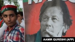 A supporter stands next to a poster of Pakistani cricketer-turned-politician Imran Khan.