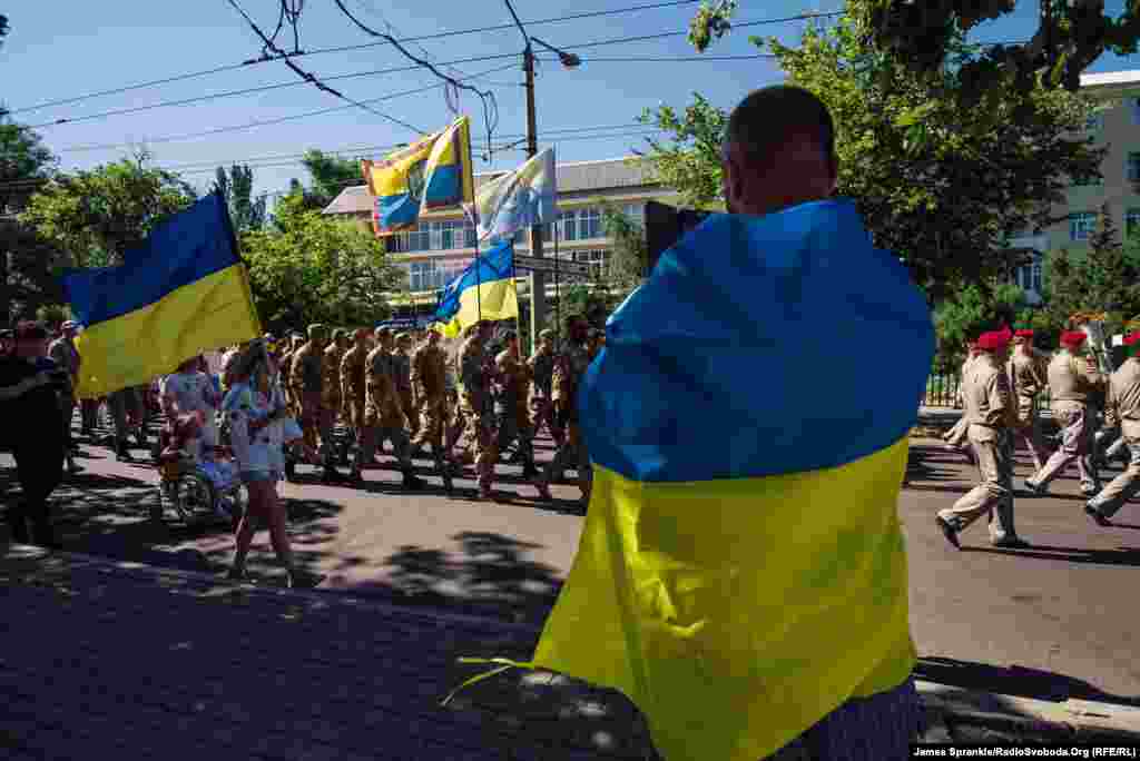 Чоловік, загорнутий в прапор, фільмує знаменну подію для міста