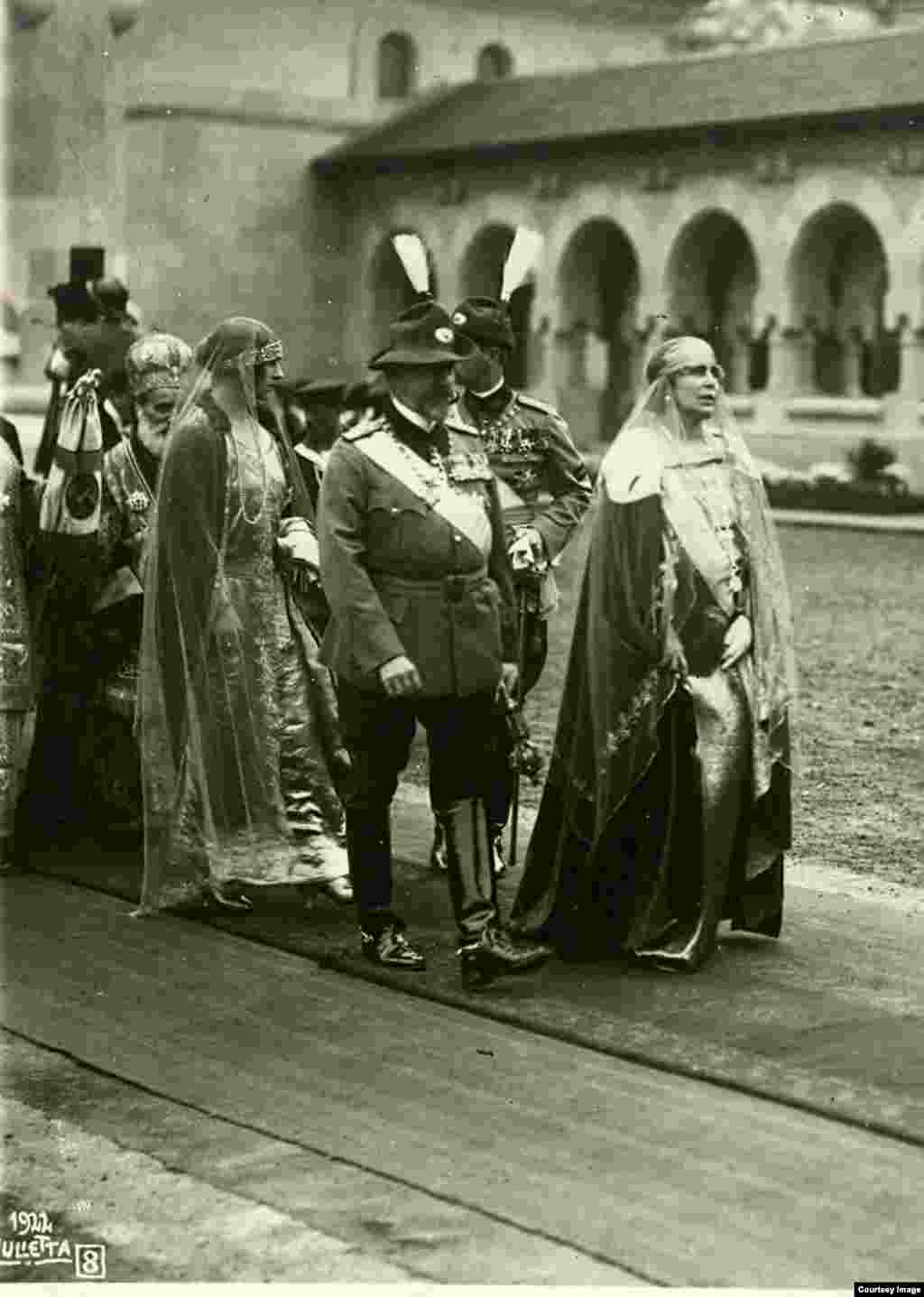 În curtea interioară a Catedralei, în drum spre Încoronare. După Regele Ferdinand și Regina Maria urmează principesele Ileana, Maria și Elisabeta și mulți oaspeți din străinătate.