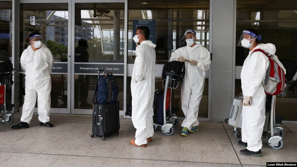 Пассажиры в международном аэропорту Сиднея в защитных костюмах