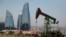 AZERBAIJAN -- Skyscrapers stand in the background as an oil pump works a nearby hill in Baku