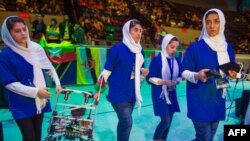 Afghan all-girls robotics team, with their robot nearby, watch other country's robots in the practice area in Washington D.C.