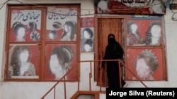 A woman wearing a niqab enters a beauty salon where the ads of women have been defaced by a shopkeeper in Kabul.

