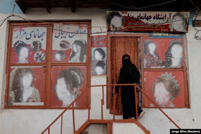 Një grua e mbuluar me nikab hyn në një sallon bukurie, ku reklamave u janë fshehur fytyrat e grave. Kabul, tetor 2021