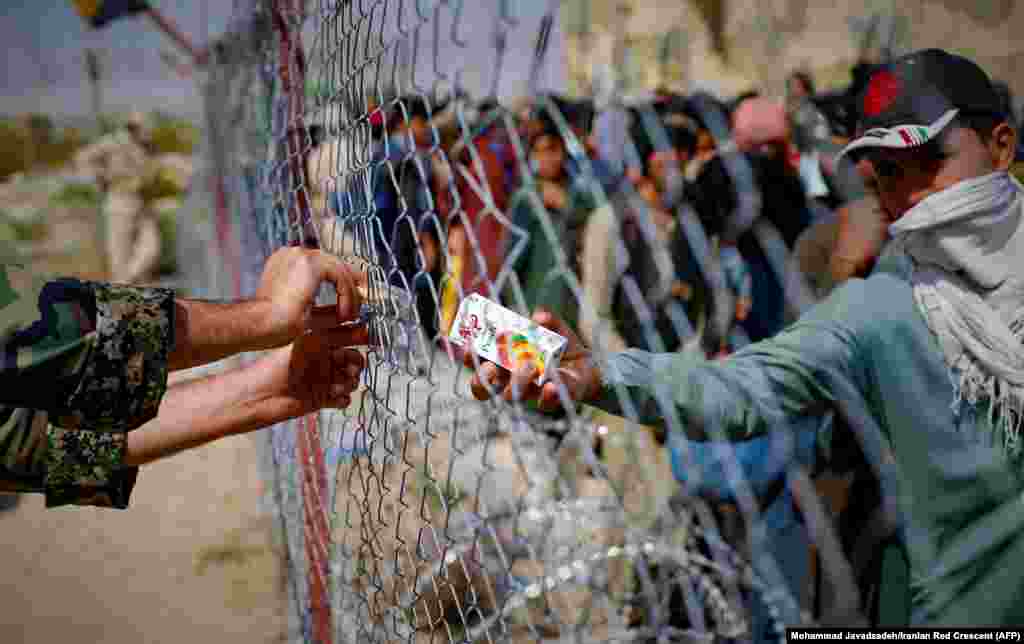 Иранский солдат раздает напитки афганским беженцам, собравшимся на ирано-афганской границе