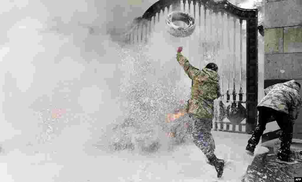 A Ukrainian serviceman throws a tire over the gates as the flames are doused by firefighters after fighters of the Aidar Ukrainian volunteer battalion burn tires at the entrance to the Ukrainian Defense Ministry in Kyiv on February 2. (AFP/Sergei Supinsky)