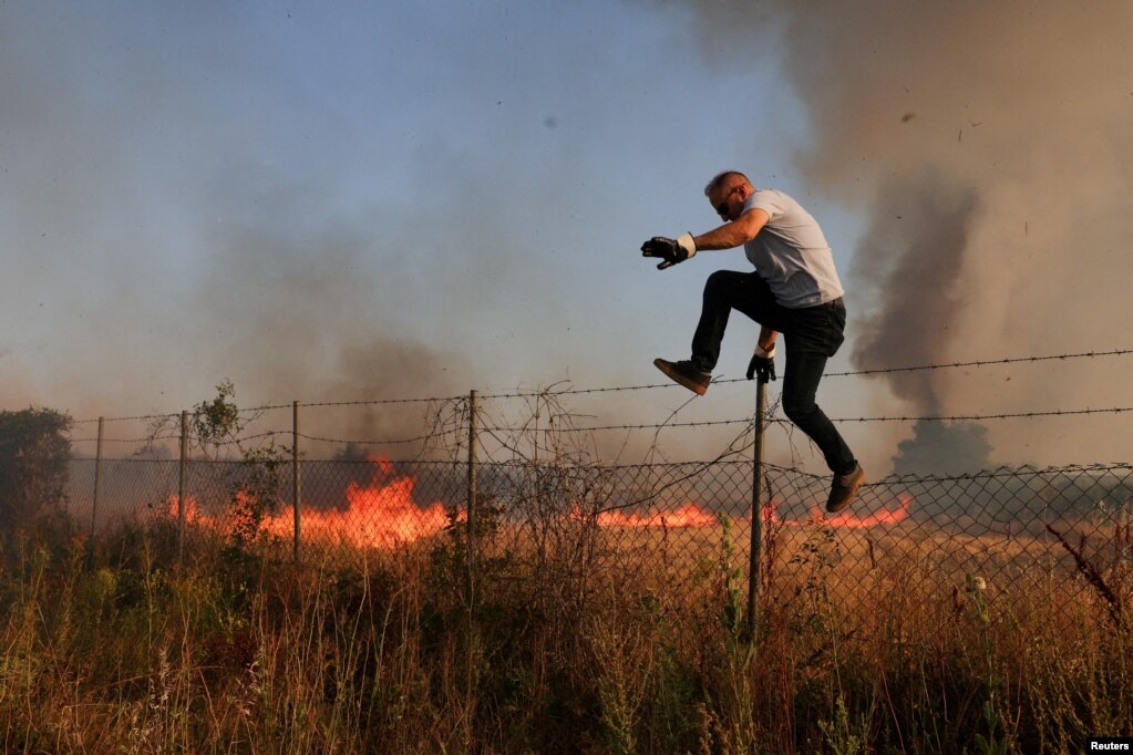 Një burrë duke kërcyer teksa flakët dhe tymi ngriheshin pas një zjarri të egër në fshatin Dubravë, në Kosovë, më 22 korrik.