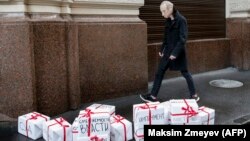 Опозициски активист со гумена маска од ликот на Путин покрај кутии со подароци на кои пишува „оставка“, „судење“ и сл.