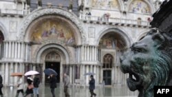 Italy -- People walk on a platform to cross Piazza San Marco (St Mark's square) flooded, Venice, 10Feb2009